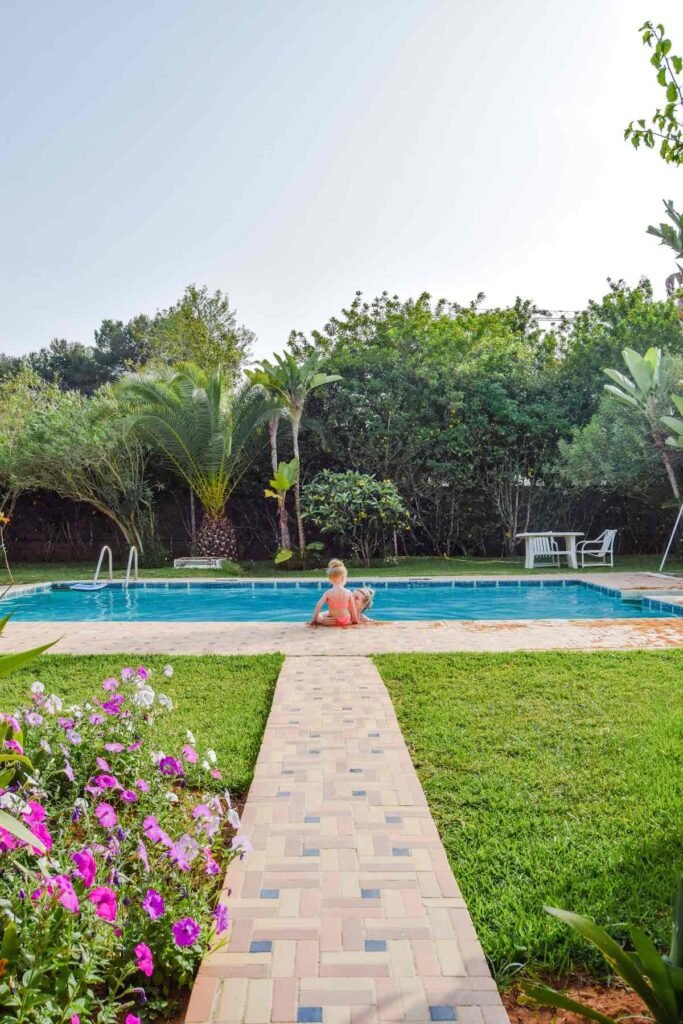 Mother and daughter sits around a Moroccan pool, surrounded by lush gardens.