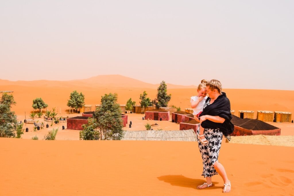 Mother and you daughter stand on a sand dune over looking Ali and Saras Desert Palace