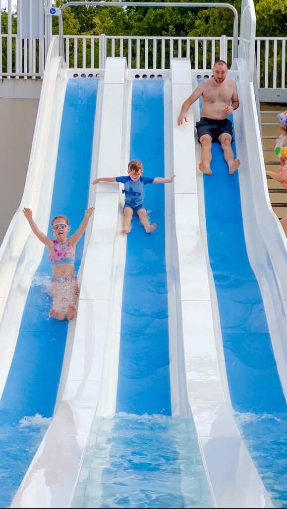 Father and 2 young children race down the water slides at Camping la Grande Tortue pool complex