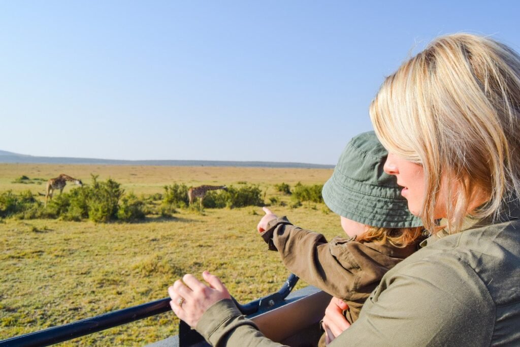 Mother and young child watch 2 giraffes from their safari jeep