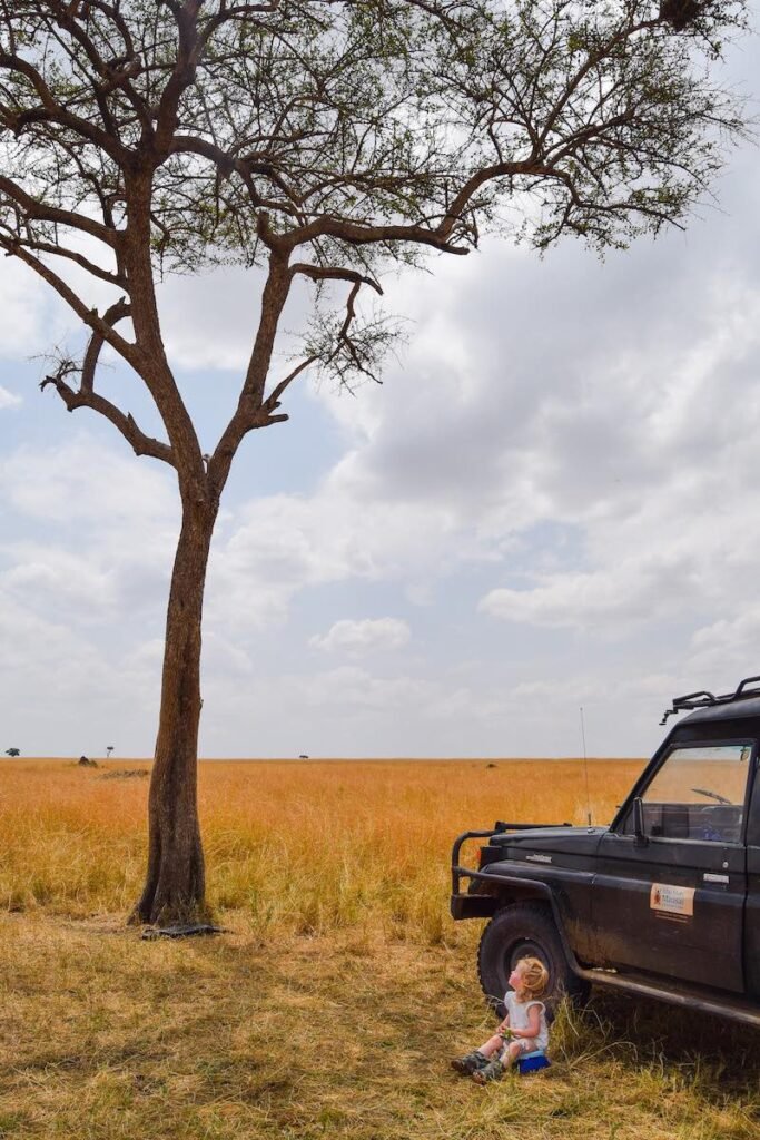 Young girl sits on a travel potty, under a tree, on an African safari in the Masai Mara