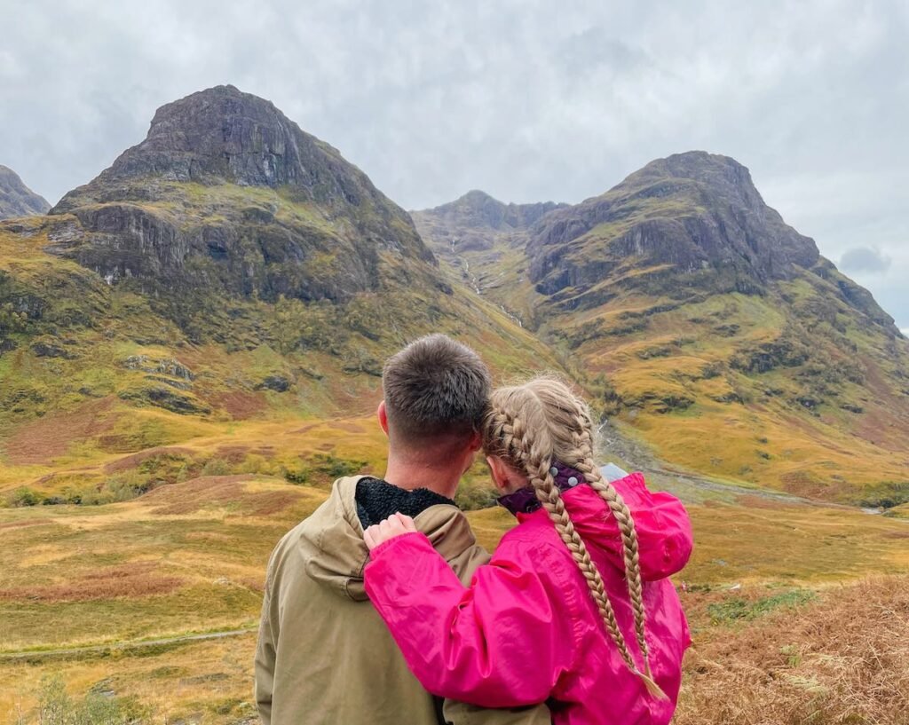 Father and daughter hug whilst looking out over Glen Coe, three sisters