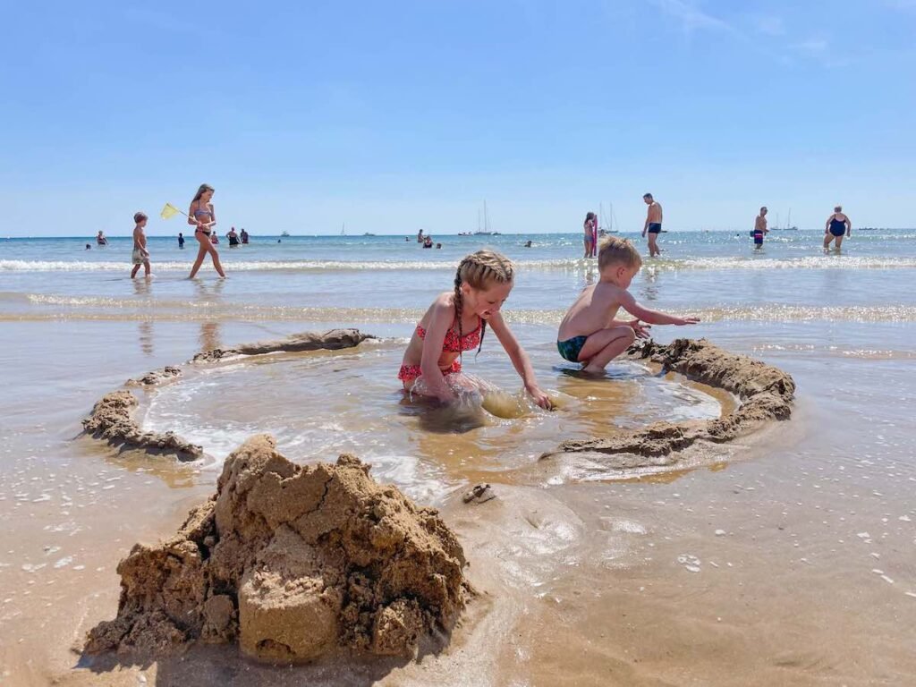 Children play in the sand at Les Sables D’Olonne beach, digging a whole and filling it with water