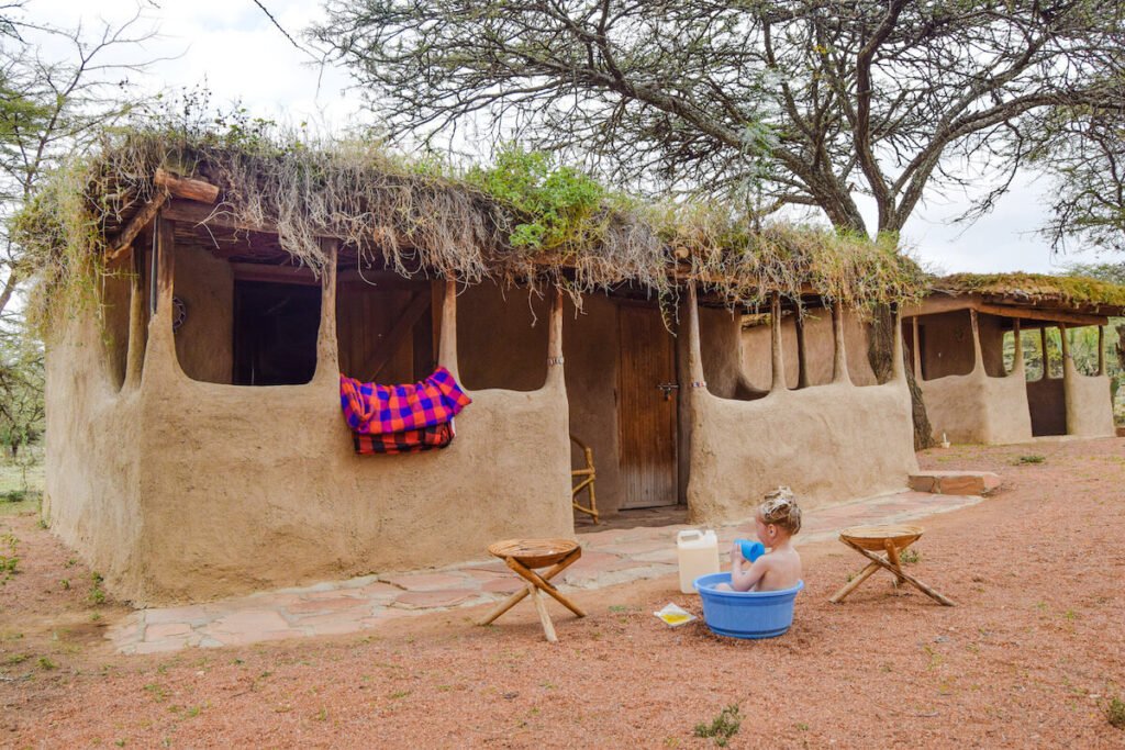 Maasai manyatta hut Maasai Tribe at Maji Moto Maasai Cultural Camp, with a child bathing in a small plastic tub