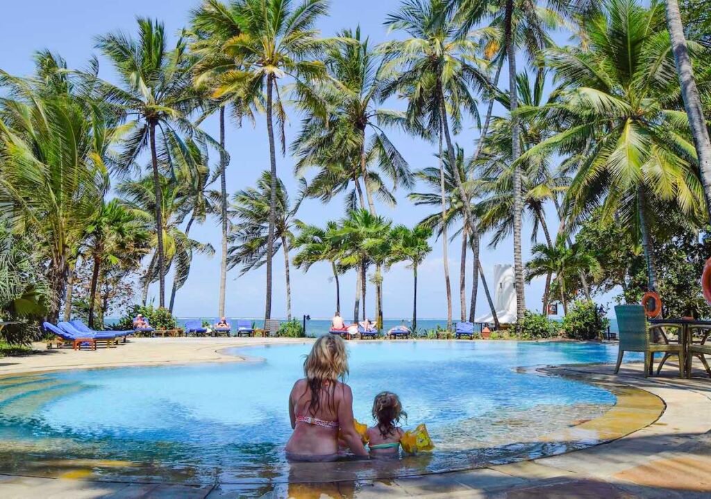 Mother and young child sit in the pool at Severin Sea Lodge. with palm trees above their heads and clear blue sky